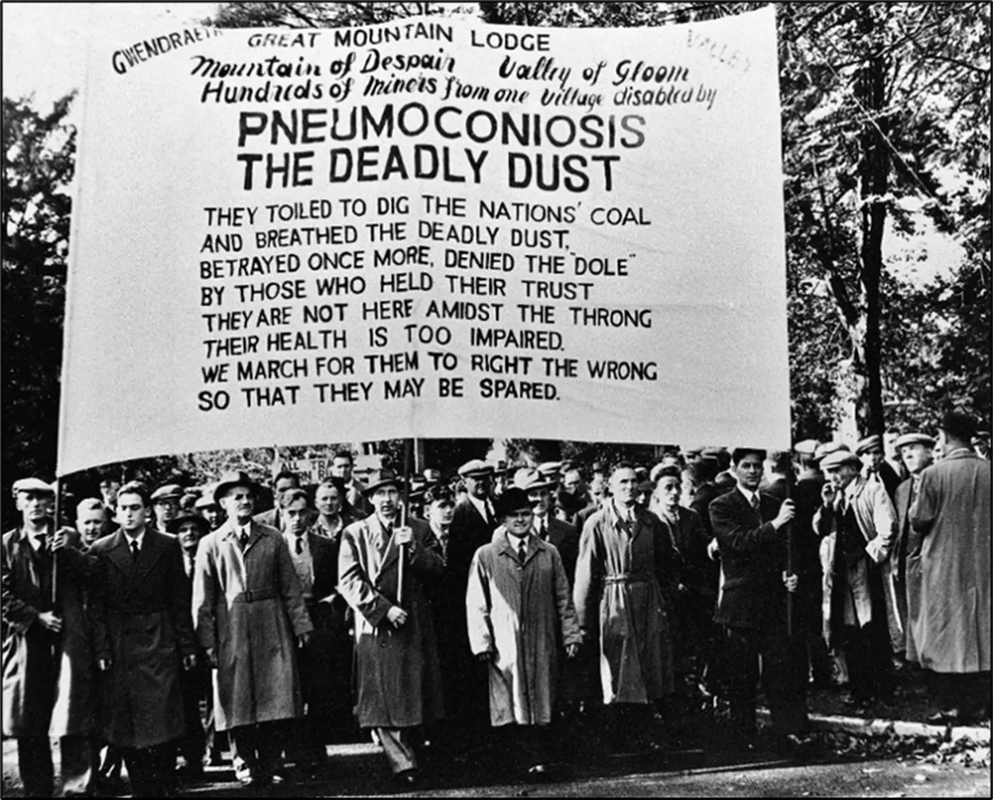 Great Mountain miners in the 1950s marching behind a banner reading Pneumoconiosis — the deadly dust