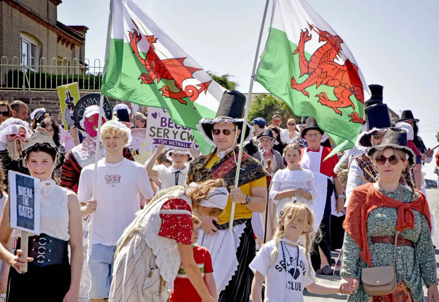 Families and children in Rebecca costume carrying Welsh flags and banners at Gwyl Tyisha